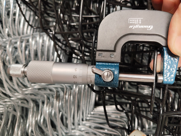 Micrometer measures wire diameter of chain link fence for quality inspection.