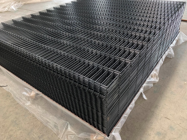 Stacked black 2D fence panels neatly placed on protective film in factory workshop.
