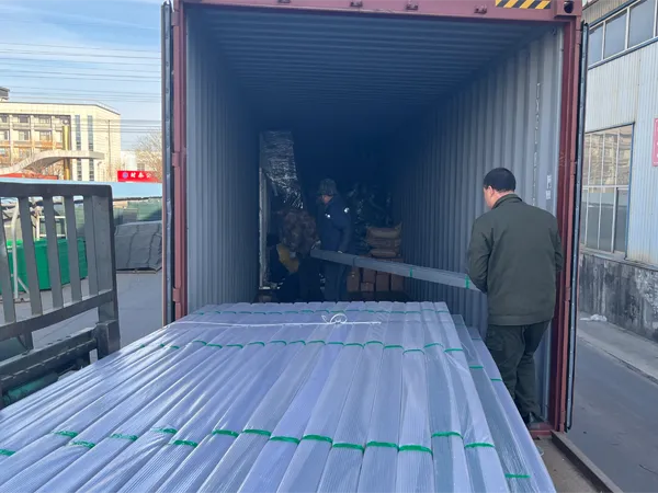 Workers load goods, including 358 security fence materials, into a container at a factory yard.