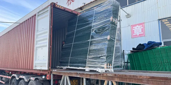 A pallet of wrapped 358 security fence is being loaded into a container at a factory.