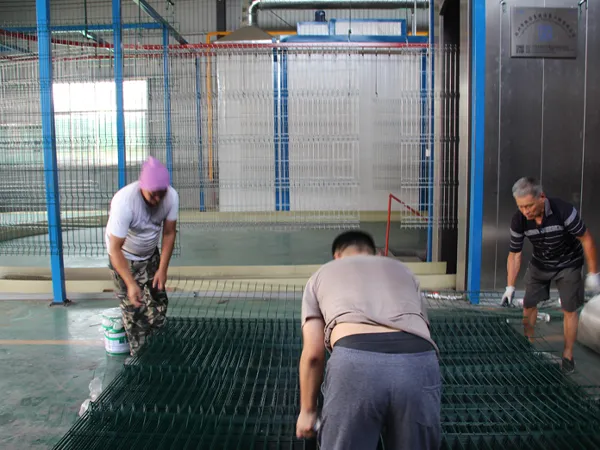 Workers are applying powder coating to a 3D fence panel.