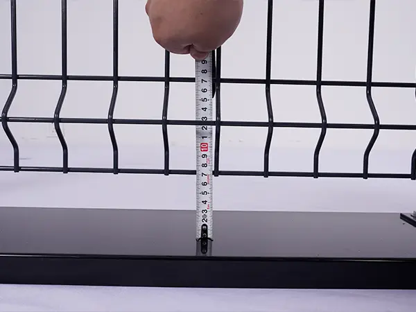 A QC worker is measuring the distance between fence panel and ground.