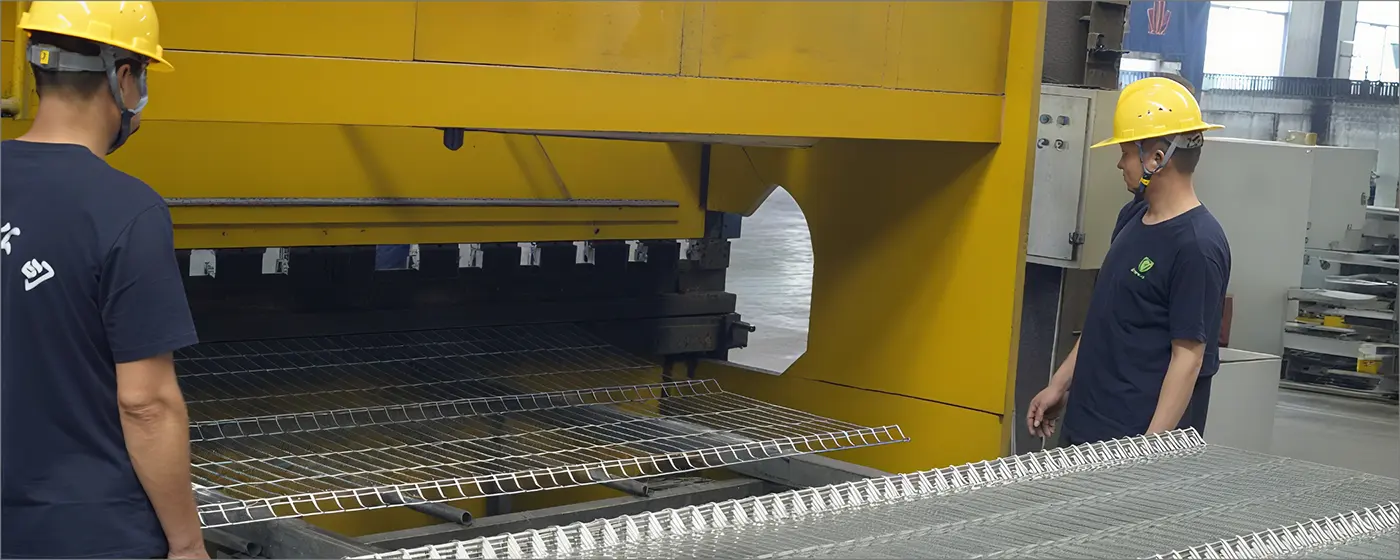 Two workers are standing and operating the bending machine of 3D security fence.