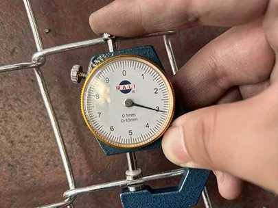 A QC worker is measuring the wire diameter of American temporary fence with caliper.