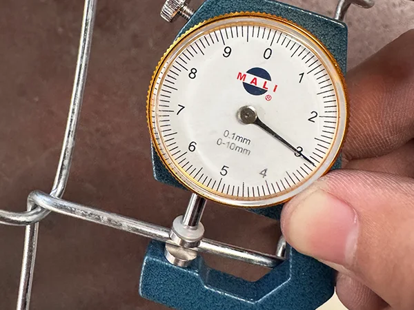 A QC worker is measuring the wire diameter of chain link fence.