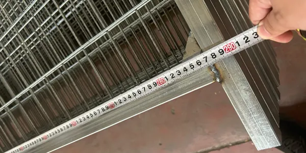 Galvanized Canada temporary fence, measuring overall panel length with tape measure in workshop