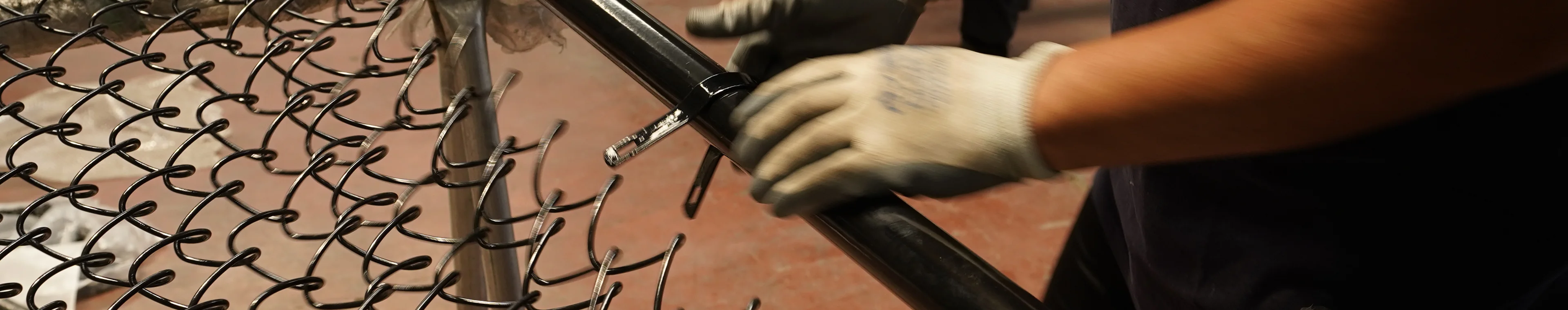 Рабочий собирает забор из звеньев цепи.