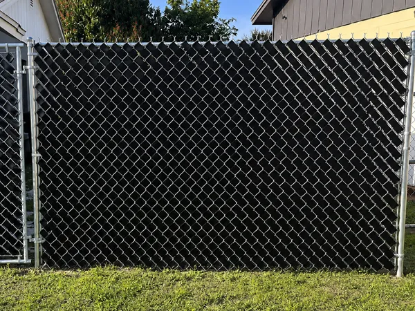 Chain link fence with privacy tape installed around a garden area.