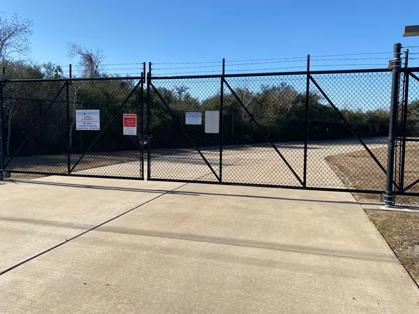 Black chain link fencing system gates secure a water facility with warning signs and barbed wire.