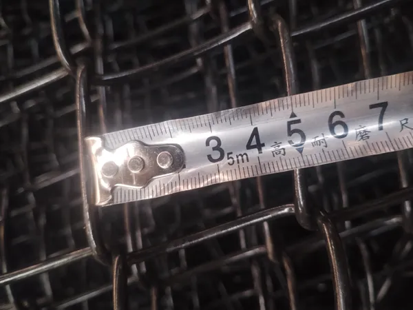 A tape measure checks the mesh opening size of the chain link fencing system.