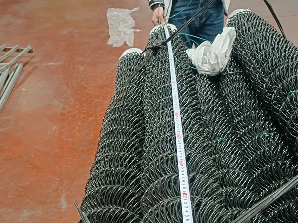 A worker measures a roll of black coated chain link fencing system with a tape measure in the factory.