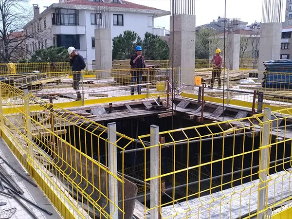 The yellow edge protection barriers are surrounding the deep excavation pit and workers are working.
