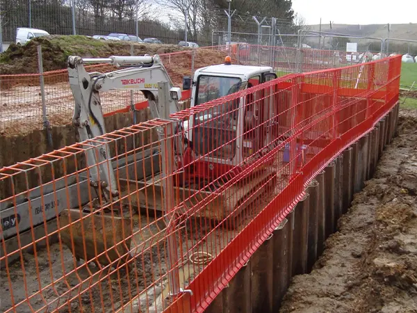 The red edge protection fences are surrounding the construction site and a forklift is working in it.
