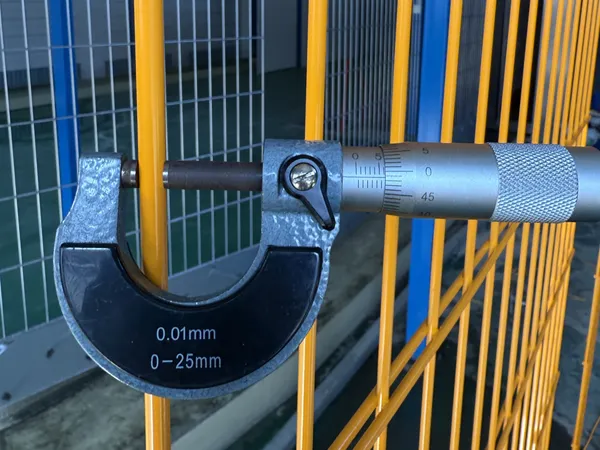 Worker using a micrometer to measure edge protection fence metal rod diameter