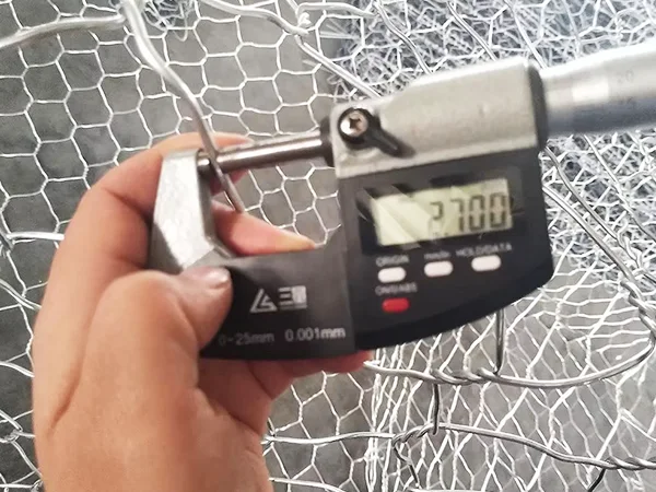 A QC worker is measuring the mesh wire diameter of woven gabion retaining wall.