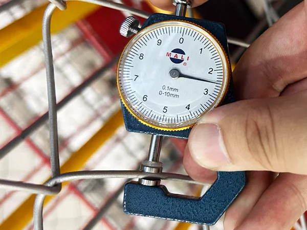 A QC worker is measuring the wire diameter of Galvanized New Zealand temporary fence.