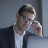 A Germany business man is watching computer with his hand holding the glasses.