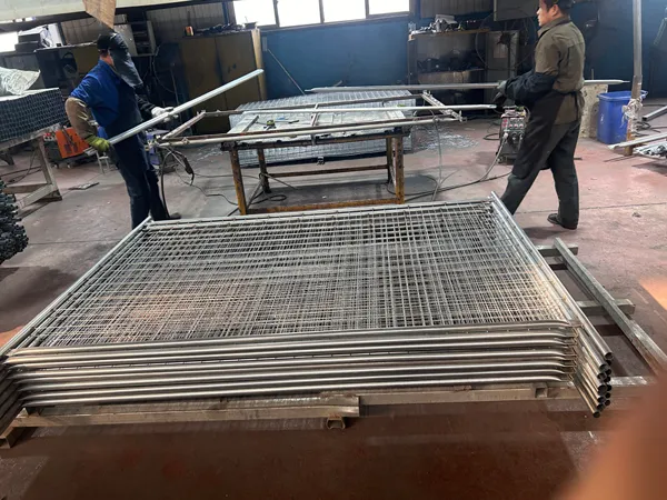 Factory workers assemble large metal mesh fence panels in a workshop, with finished Giant Fence frames ready for further processing.