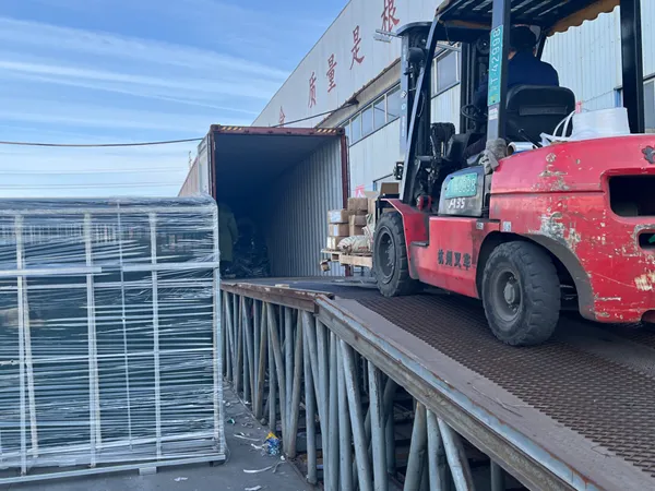 A red forklift loads wrapped Giant Fence panels and boxes into a shipping container at a factory yard, ready for export.