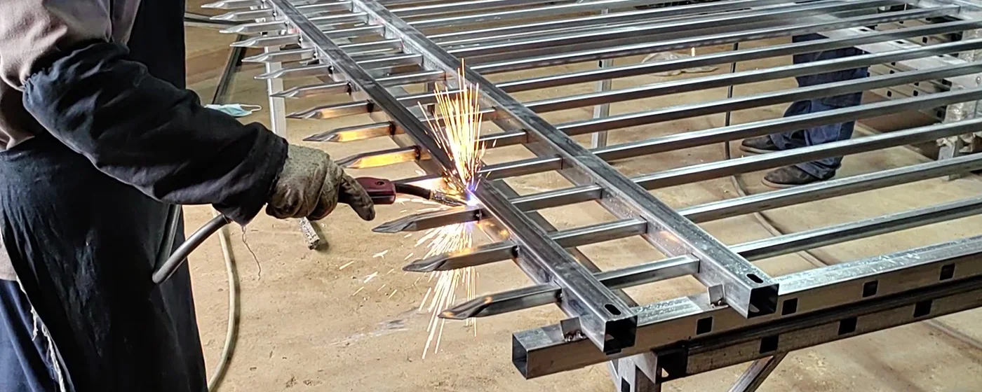 A worker is welding pickets onto rails of steel tubular fence.